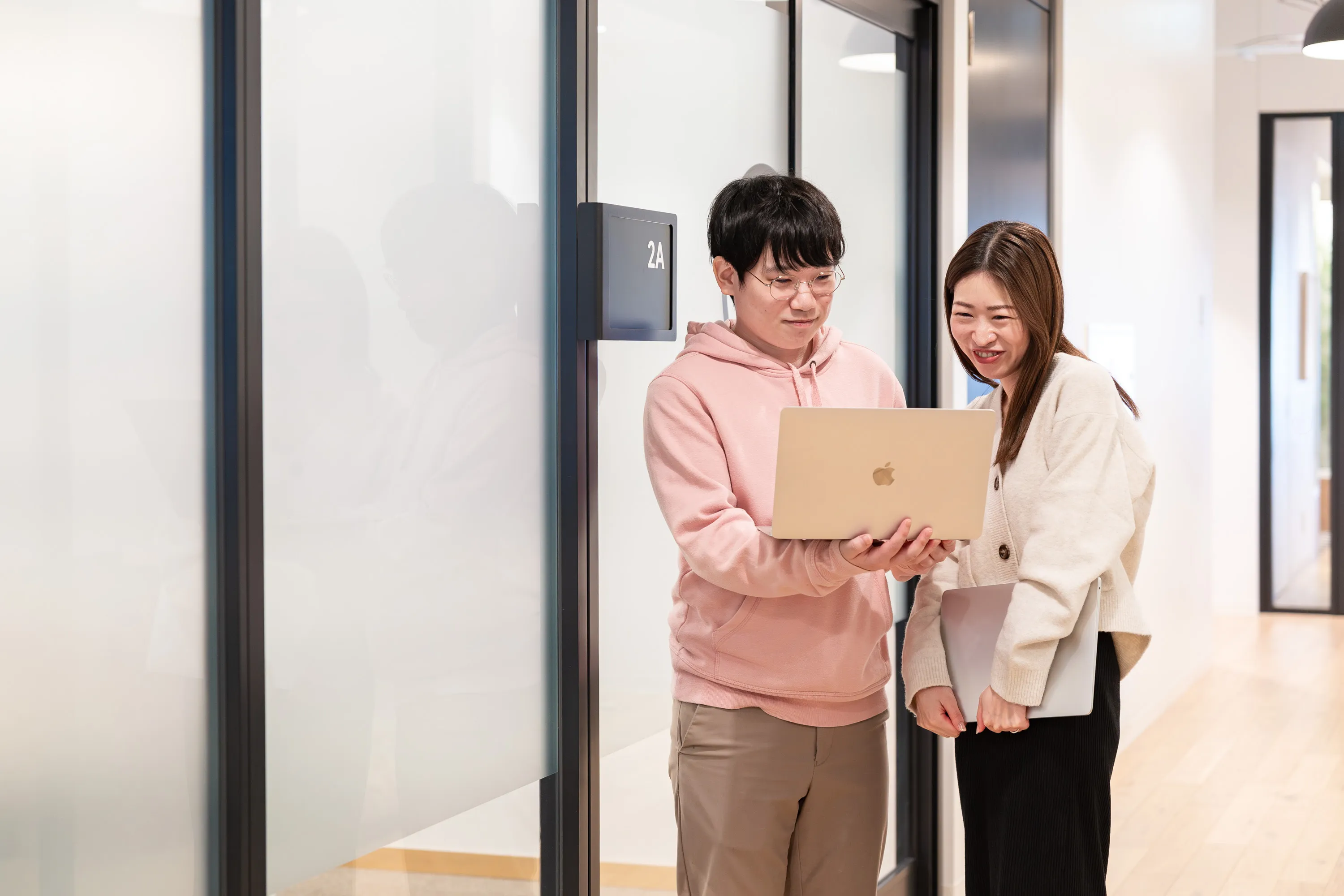 男性が片手にPCを持ち、女性と一緒にPCの画面を見ながら話している写真